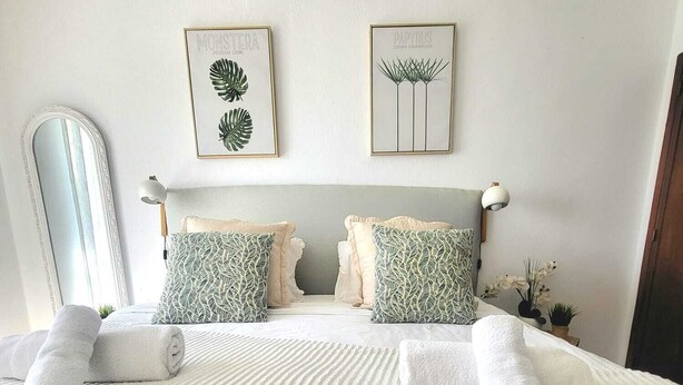 A bedroom with a large bed, two pillows, a headboard, a mirror, and two framed botanical prints on the wall. - CHABELLA! Charm Beach Lofts Apartments - Garden & Sea View - CARVOEIRO - ALGARVE (Carvoeiro)