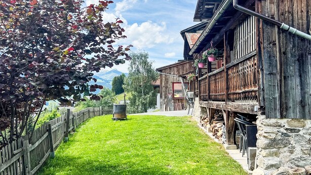 Ein rustikales Holzgebäude mit Steinuntergrund, Holzzaun und Rasenfläche.