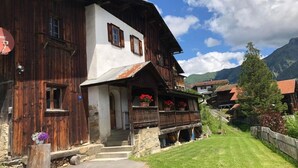 Ein traditionelles Holzhaus mit weißer Fassade, einem Balkon voller Blumen und einer Steintreppe, die zum Eingang führt.