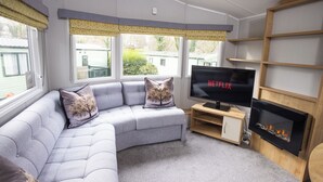 A living room with a grey sectional sofa, a flat-screen TV, a fireplace, and large windows with curtains. - The Lake House - Quiet, Dog Friendly, By the Lake, Free Parking (Bowness-on-Windermere)