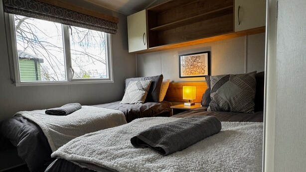 A bedroom with two beds, a nightstand with a lamp, a window with a view, and a wooden shelf above the beds. - The Lake House - Quiet, Dog Friendly, By the Lake, Free Parking (Bowness-on-Windermere)