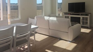 Een ruime woonkamer met een witte bank, een eettafel met stoelen, een plafondventilator en een televisie op een kast.