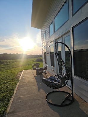 Un patio con mobiliario exterior, incluyendo una silla y una mesa, cerca de un edificio con ventanales amplios.
