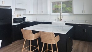 Een moderne keuken met witte kastjes, zwarte apparaten en een groot eiland met twee rieten stoelen.