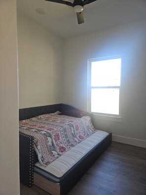 A room with a single bed, a window, and a ceiling fan.