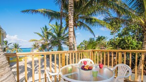 A wooden deck with a glass table and white chairs, overlooking a beach with palm trees and the ocean. - Cottage By The Sea ~Wonderful Family Friendly 2-bedroom with AC in East End (East End)