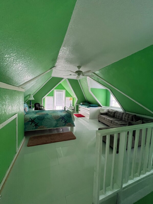 A room with a sloped ceiling, a bed with a star-patterned bedspread, a white dresser, a red rug, and a white crib.