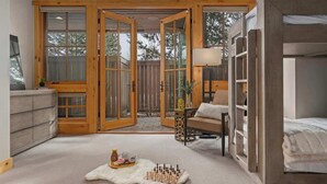 A room with a large sliding glass door leading to an outdoor area, a bed with a headboard, a small table with a lamp, and a fur rug on the floor. - Abode at Elkhorn Village, hot tub, steps to skiing (Sun Valley)