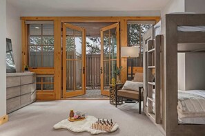 A room with a large sliding glass door leading to an outdoor area, a bed with a headboard, a small table with a lamp, and a fur rug on the floor.