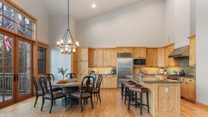 A spacious kitchen with wooden cabinets, a stainless steel refrigerator, and a dining area with a chandelier. - Abode at Elkhorn Village, hot tub, steps to skiing (Sun Valley)