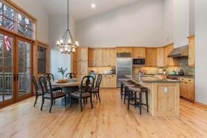 A spacious kitchen with wooden cabinets, a stainless steel refrigerator, and a dining area with a chandelier. - Abode at Elkhorn Village, hot tub, steps to skiing (Sun Valley)