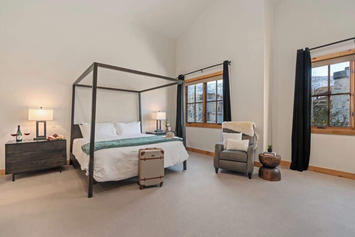 A four-poster bed with a suitcase, a chair, and a window with a view.