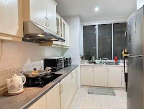 Une cuisine moderne avec des meubles blancs, un réfrigérateur en acier inoxydable, une cuisinière à gaz et un four à micro-ondes.