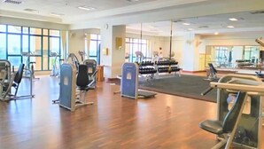 Et stort fitnessrum med forskellig træningsudstyr, store vinduer og trægulv.