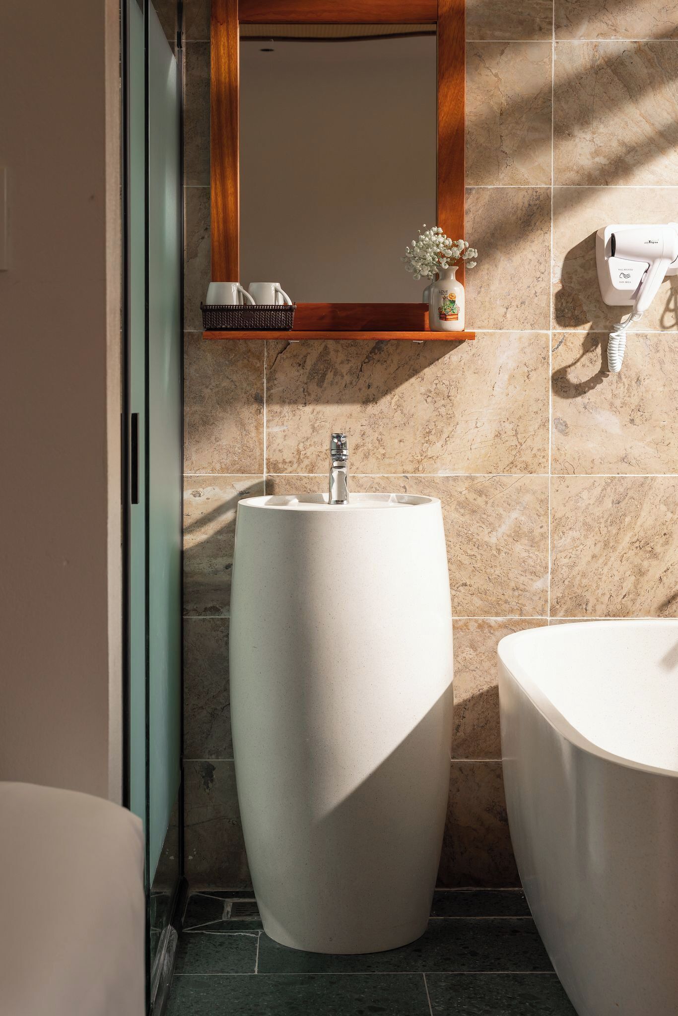 A bathroom with a large, round sink, a mirror with a wooden frame, and a hairdryer mounted on the wall.