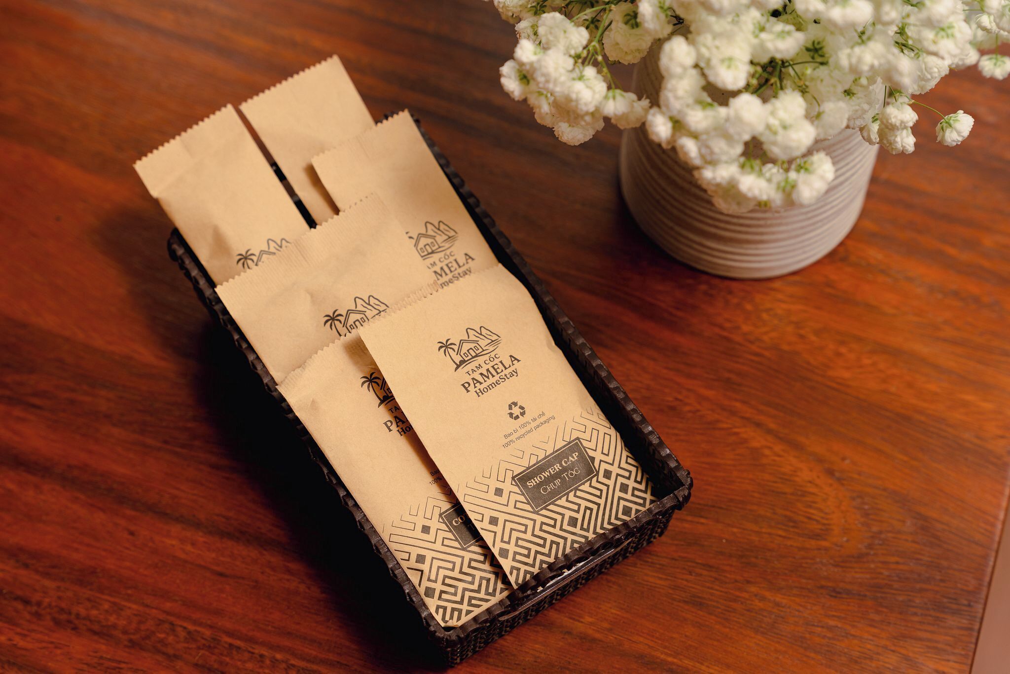 A wooden tray with two paper bags labeled "Pamela Homestay" and "Shower Cap."