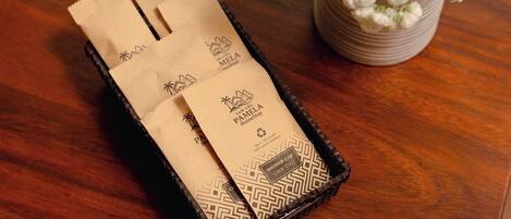 A wooden tray with two paper bags labeled "Pamela Homestay" and "Shower Cap."
