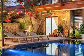 Un espace aménagé au bord de la piscine, avec des chaises longues, un mur en pierre et une porte portant l’inscription « 102 ».