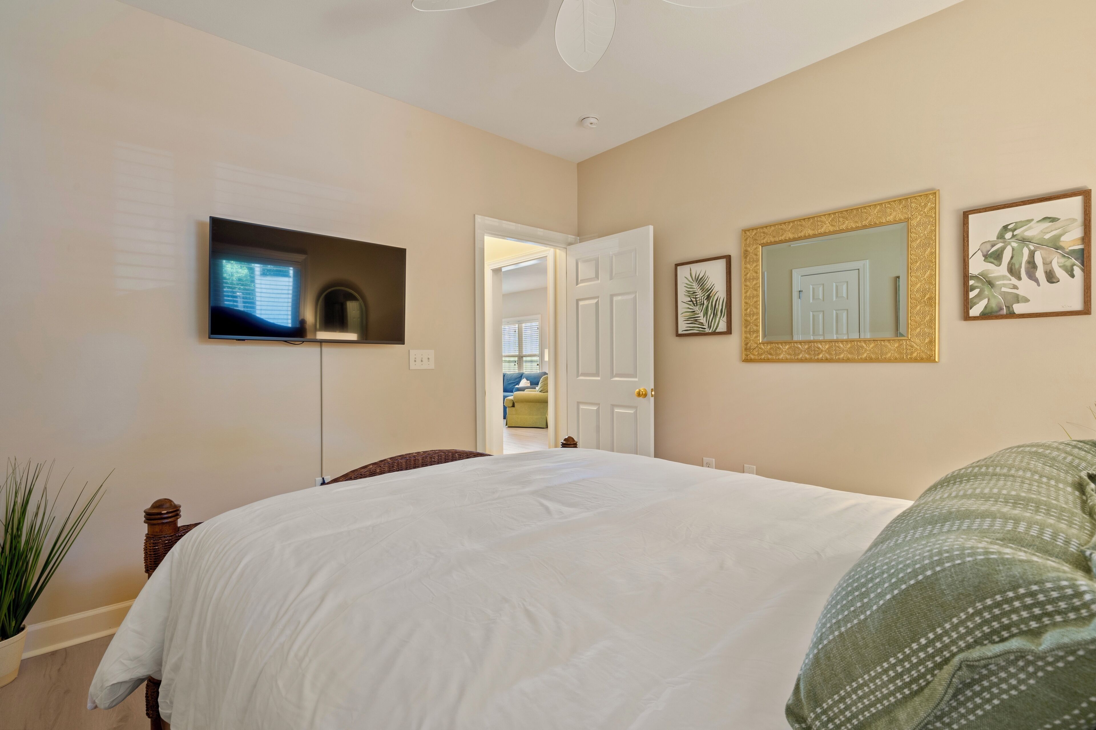 A bedroom with a large bed, a TV mounted on the wall, and a door leading to another room.