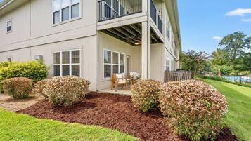 A two-story building with a balcony, a covered patio area with outdoor furniture, and a well-maintained garden with mulch and shrubs.