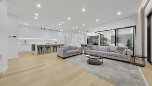 Un salon moderne avec un canapé gris, une table basse et un coin cuisine doté de meubles blancs et de tabourets de bar.