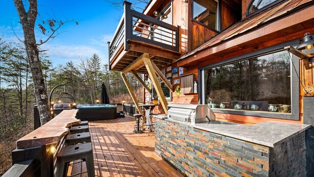 A wooden deck with a stone wall and a hot tub. - Bigfoot's Hideout - Treehouse, Arcade, Hot Tub (Blue Ridge)