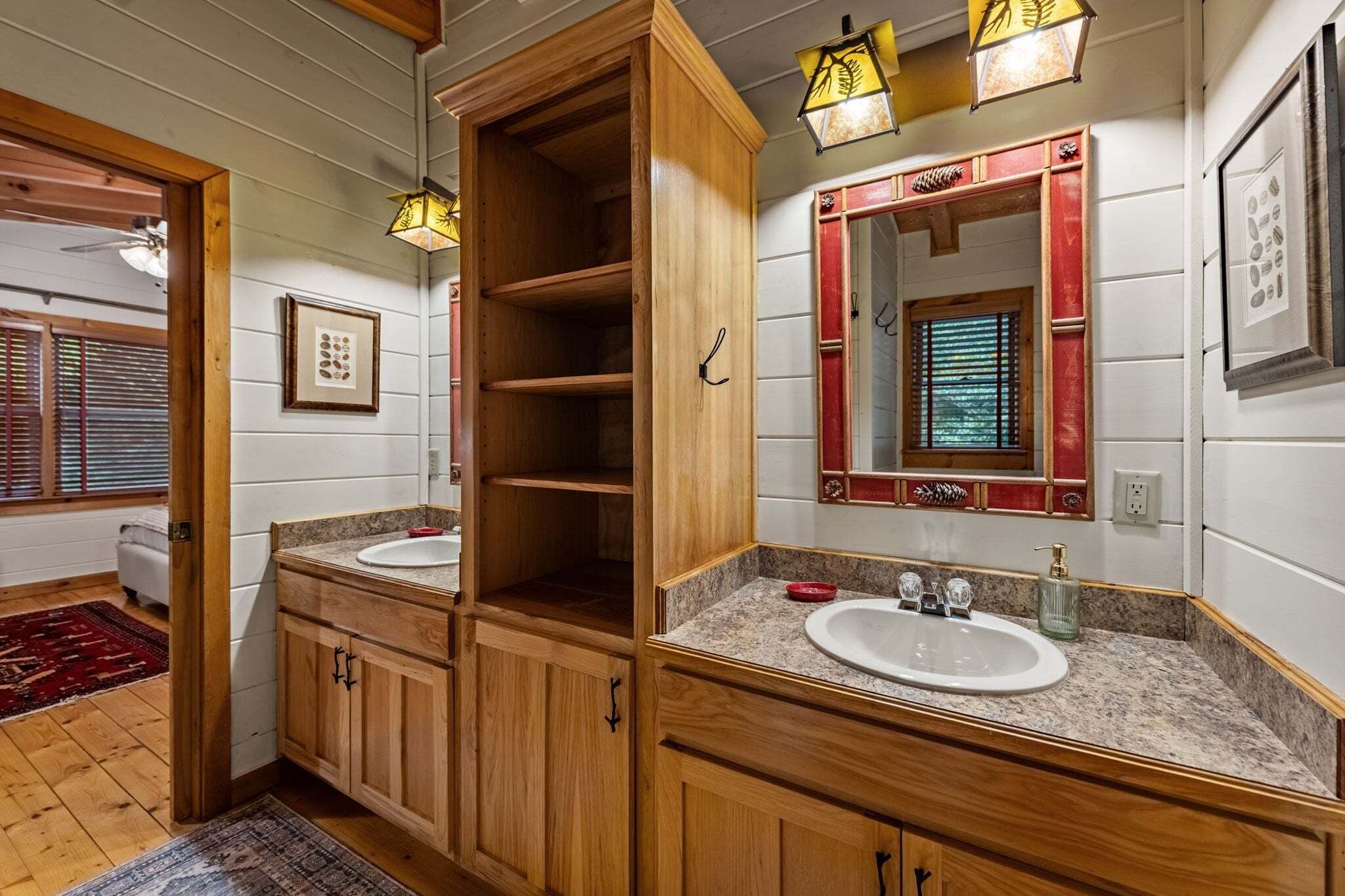 Un bagno con mobili in legno, due lavandini, uno specchio con cornice decorativa e una finestra con persiane.