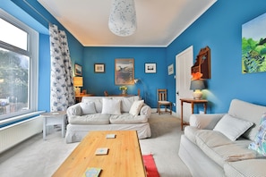 A living room with a blue wall, two sofas, a coffee table, and a dining area with a table and chairs.