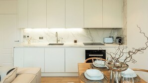 Uma cozinha moderna com armários brancos, bancada de mármore e forno embutido.