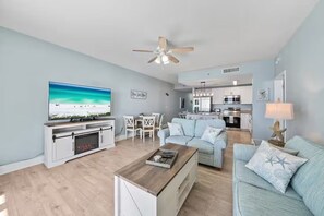 Ein modernes Wohnzimmer mit Fernseher, Kamin, Essbereich und einer Küche im Hintergrund.