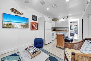 A compact living space with a kitchen, dining area, and a large TV displaying a beach scene. - Sanddollar 19B* Directly On The Beach! Amazing Views*Private Beach* (Miramar Beach)