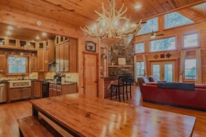 L’intérieur d’un chalet en bois comprend une grande table à manger, un coin cuisine et un espace salon confortable avec un canapé rouge.