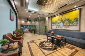A lobby with leather chairs, a sofa, a coffee table, and a painting of a woman spinning a wheel. - Ken Hotel By Connek (Hanoi)