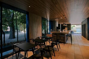 Een moderne eetruimte met een houten plafond en grote ramen met uitzicht op een tuin.