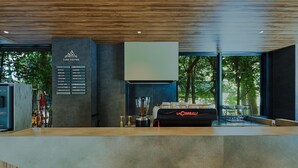 A modern coffee shop interior with a menu board, La Cimbali espresso machine, and a view of trees through large windows. - Fav Hotel Ise (Ise)