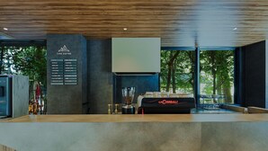 A modern coffee shop interior with a menu board, La Cimbali espresso machine, and a view of trees through large windows. - Fav Hotel Ise (Ise)