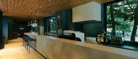 A modern bar area with a wooden ceiling, bar stools, and a counter with a coffee machine and toaster.