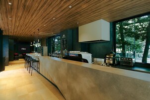 Un área de bar moderna con techo de madera, taburetes y mostrador con cafetera y tostadora.