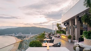 A rooftop bar with a view of the beach and mountains, featuring outdoor seating and a bar area. - Can H Du L Ch View Bi N Pullman Building (Quy Nhon)