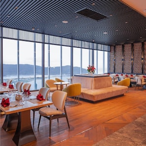 A modern restaurant with a view of the mountains, featuring wooden flooring, cushioned seating, and large windows. - Can H Du L Ch View Bi N Pullman Building (Quy Nhon)