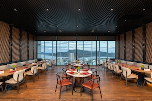 A restaurant with a high ceiling and large windows offering a view of the city. Tables are set with red napkins and centerpieces. - Can H Du L Ch View Bi N Pullman Building (Quy Nhon)