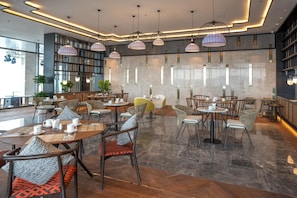 A modern cafe with multiple seating areas, including round tables and chairs, and pendant lighting. - Can H Du L Ch View Bi N Pullman Building (Quy Nhon)