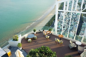 A rooftop terrace with a view of the beach and cityscape, furnished with outdoor seating and potted plants. - Can H Du L Ch View Bi N Pullman Building (Quy Nhon)