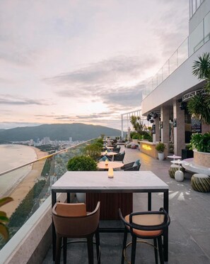 A rooftop bar with a view of the beach and mountains, featuring outdoor seating and a bar area. - Can H Du L Ch View Bi N Pullman Building (Quy Nhon)