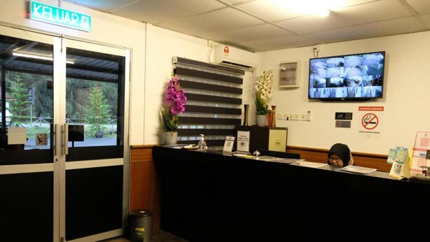 Un área de recepción con mostrador negro, un televisor montado en la pared y un letrero que dice 'KELUAR'.
