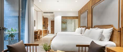 Una habitación de hotel moderna con una cama grande, muebles de madera, una mesita con un florero y un libro, y un balcón con plantas.