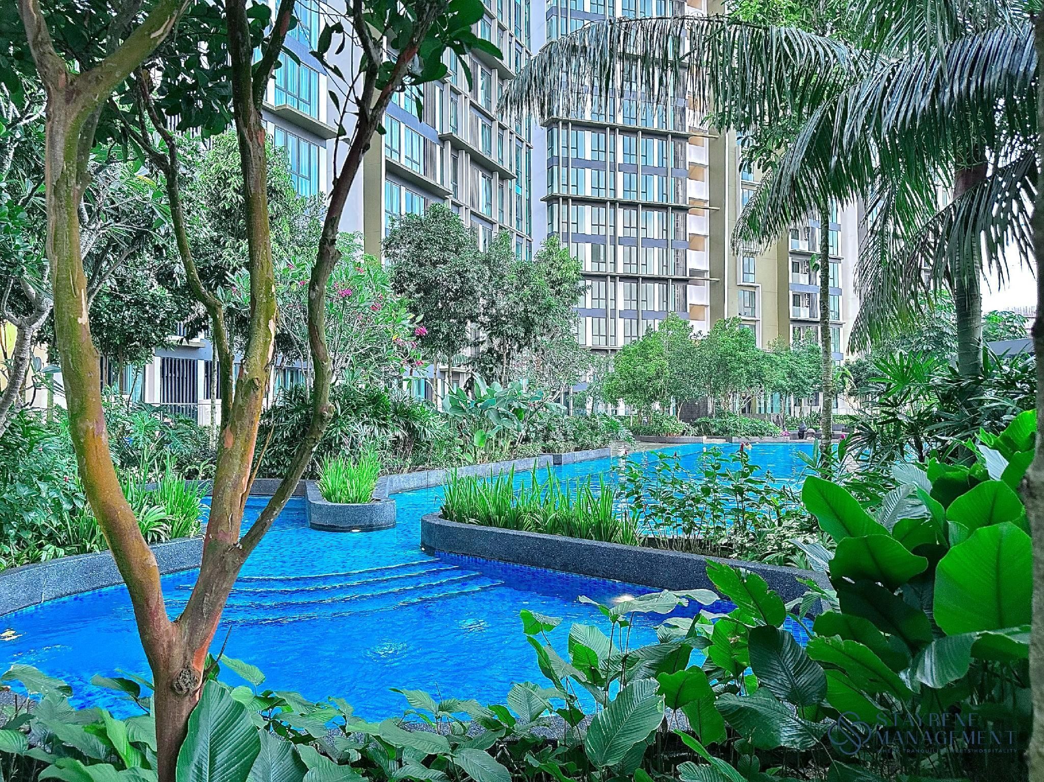 A pool surrounded by lush greenery and modern buildings in the background.