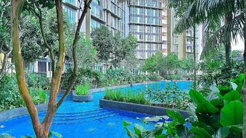 A pool surrounded by lush greenery and modern buildings in the background.
