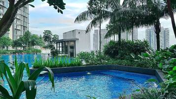 A swimming pool surrounded by lush greenery and tall buildings in the background.
