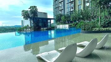 A swimming pool with lounge chairs, surrounded by greenery and modern buildings.